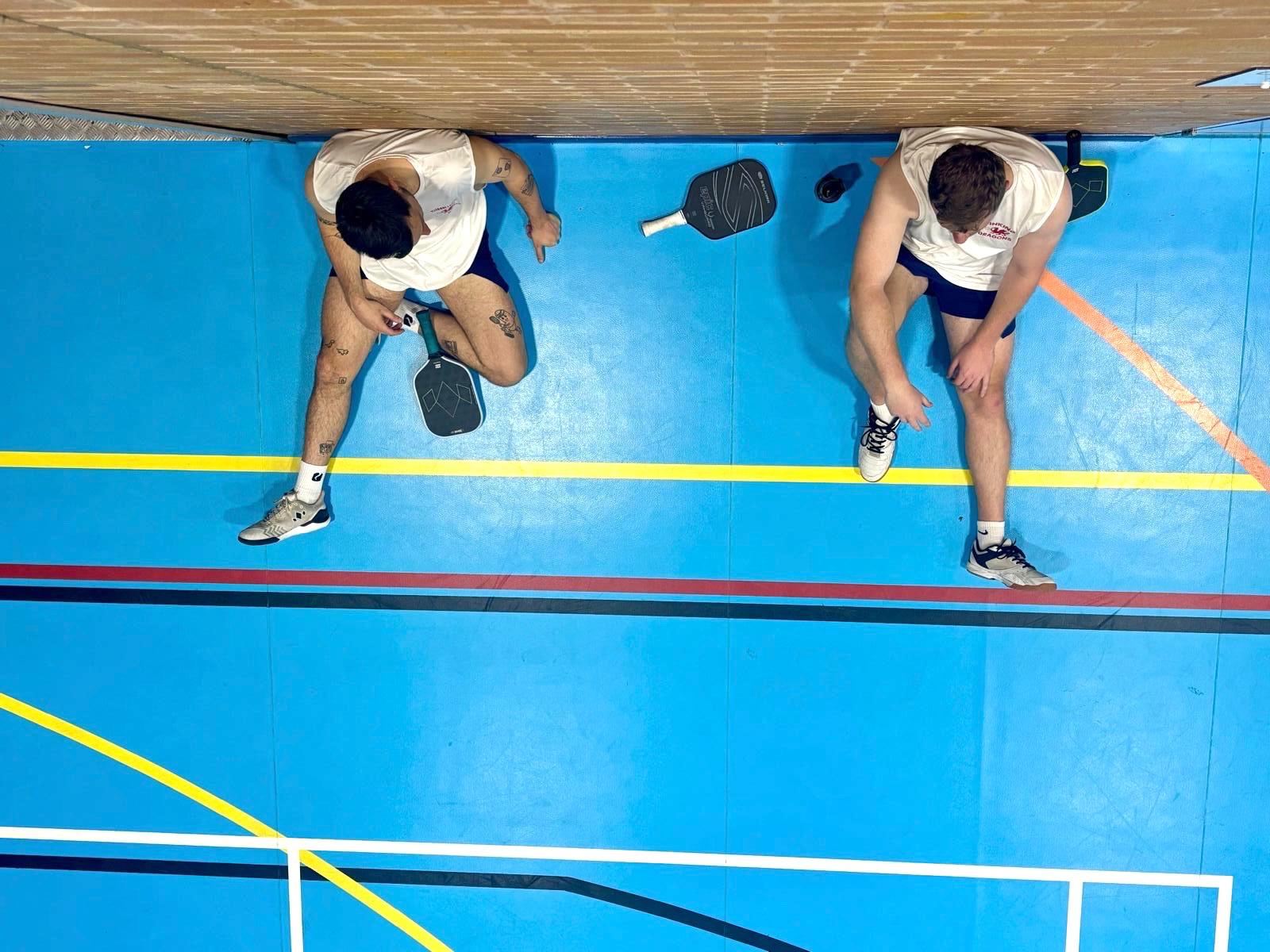 Two pickleball players seen from above on an indoor court