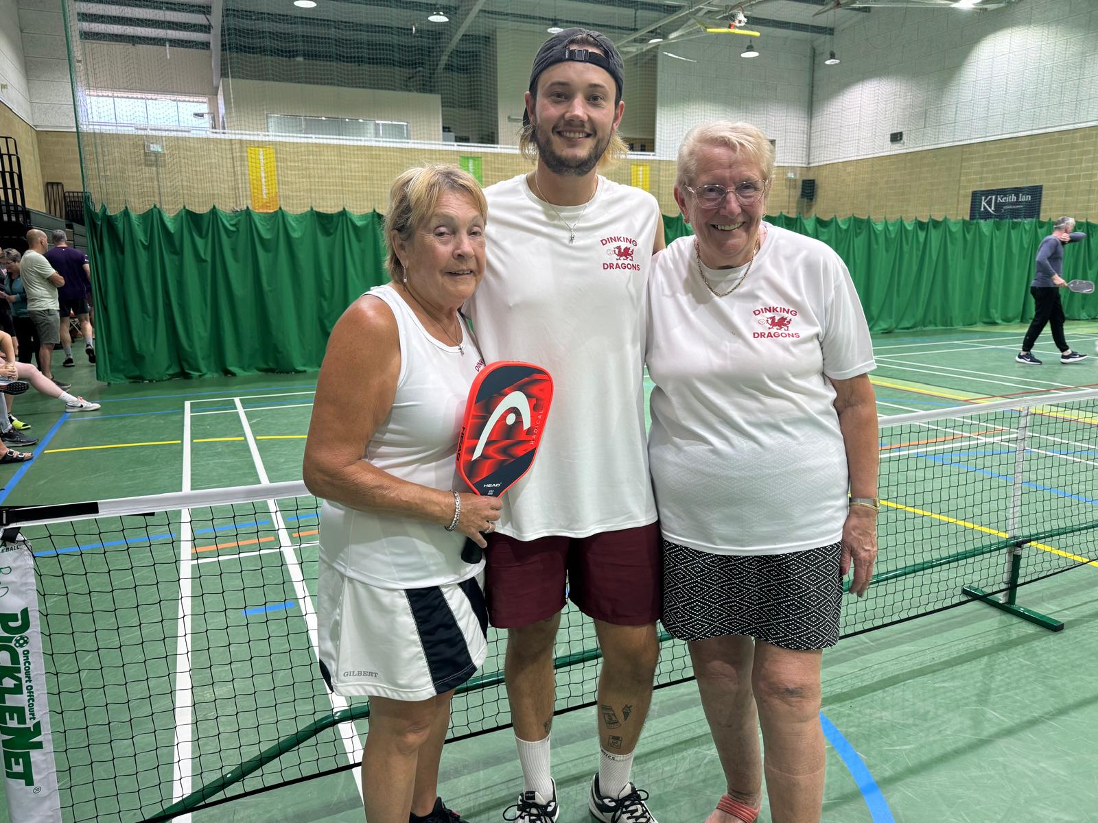 Three people posing beside an indoor pickleball net